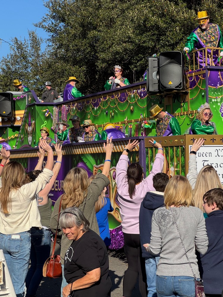 People standing in the street with hands raised with a Mardi Gras float passing by
