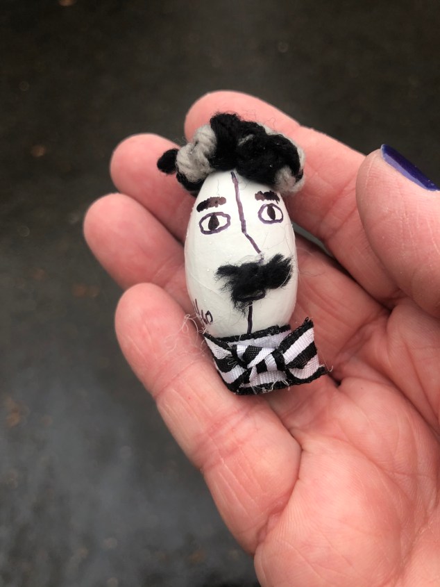 A pecan with a face painted in black and white with a bow tie added, and facial and head hair