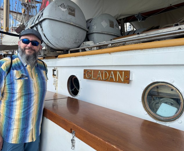 A man standing in front of the Gladan - Swedish Ship sign