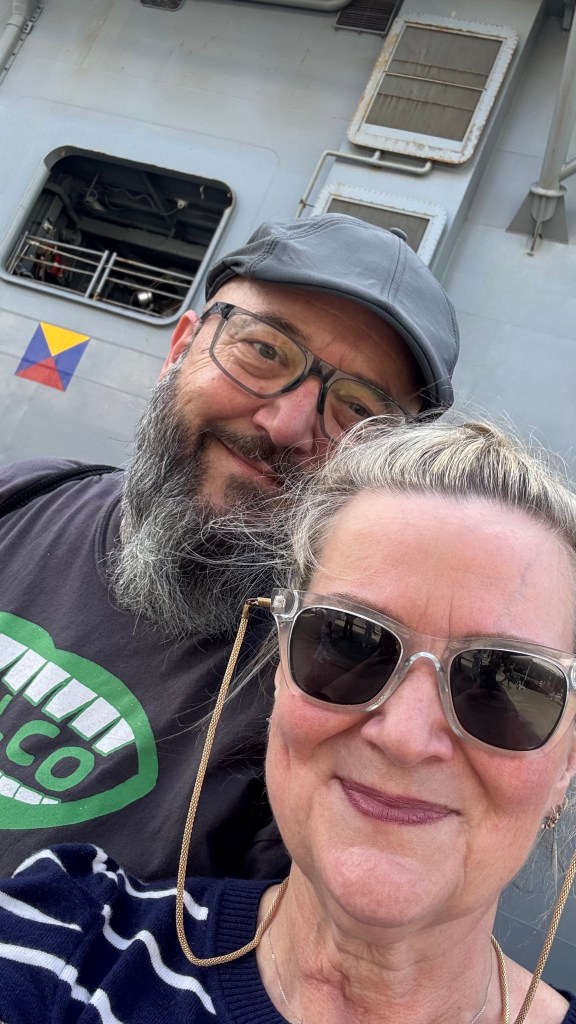 a man and woman taking a selfie in front of the USS Kearsarge