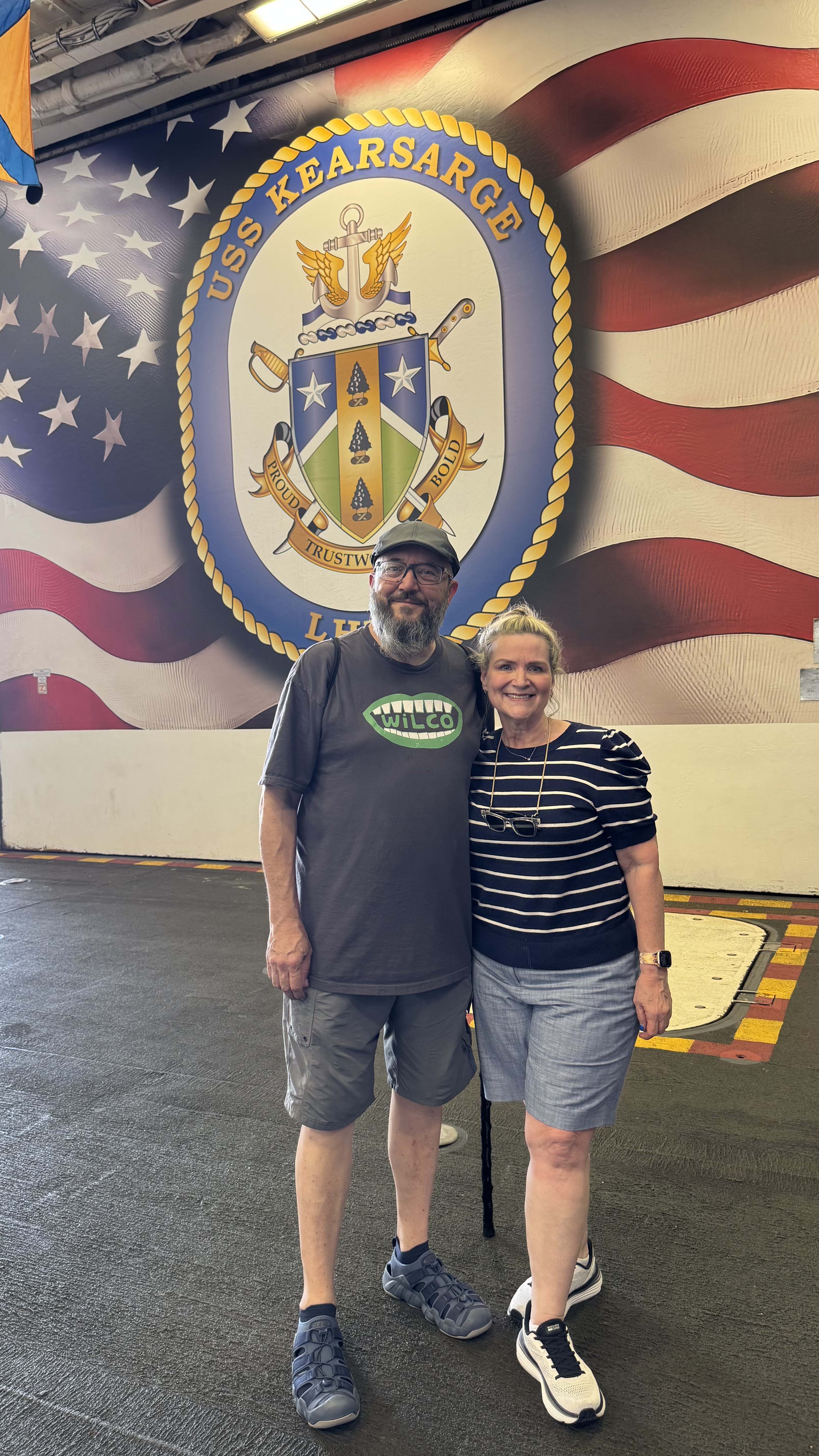 a man and woman standing in front of a painted mural on the USS Kearsarge